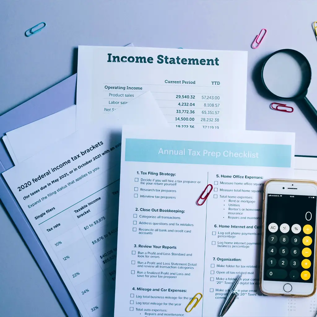 A desk with a folder of tax documents, calculator, magnifying glass and paper clips